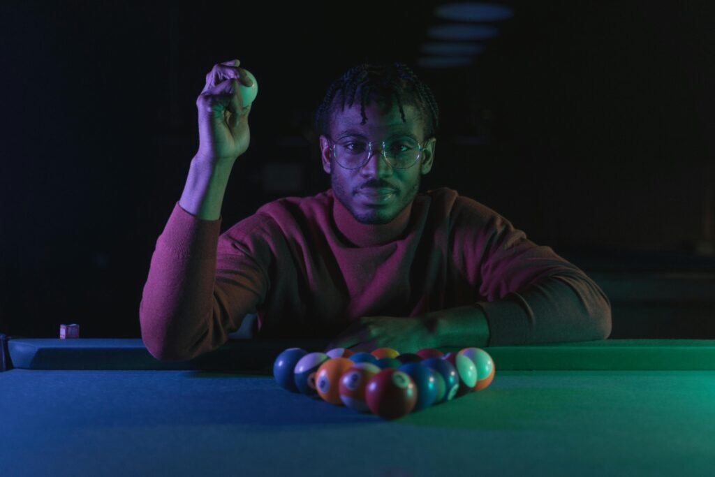 A man lines up a pool shot in a dimly lit room, holding a cue ball confidently.